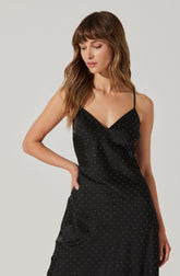 A woman is wearing a black spaghetti strap dress with small white polka dots. The dress features a V-neckline and a fitted waist.